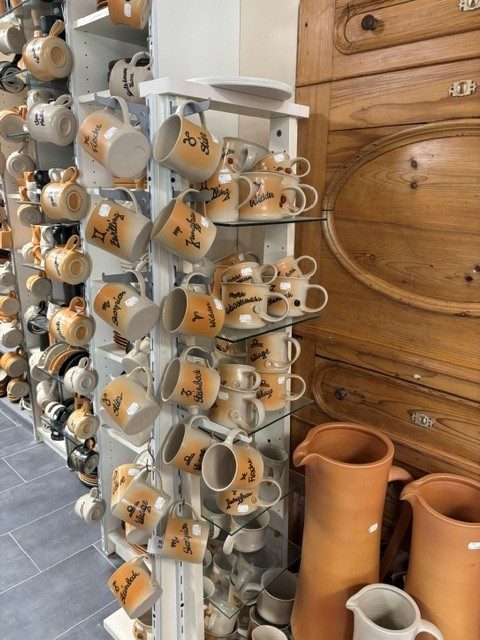 Wandregal voller Tassen mit handgemalten Namen, daneben Krüge aus Terrakotta